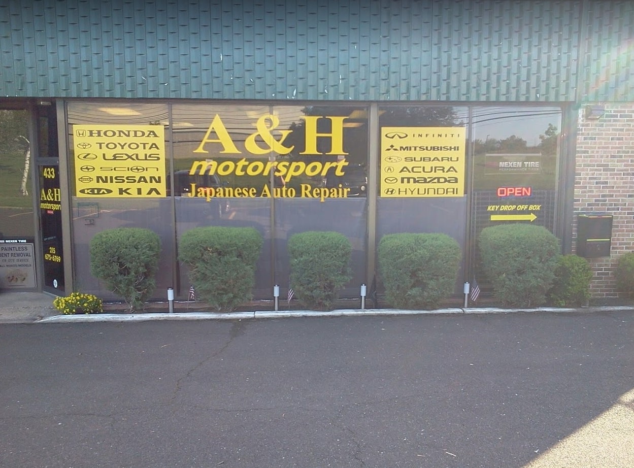 Front view of A & H Motorsport Company, featuring an open sign and displaying car brands on glass doors, along with contact details