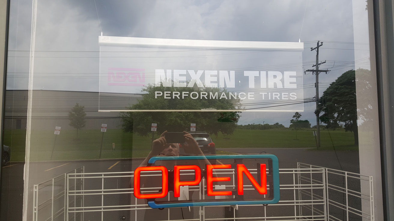 A glass door featuring the Nexen Tire Performance Tires logo, with an open sign displayed, welcoming customers